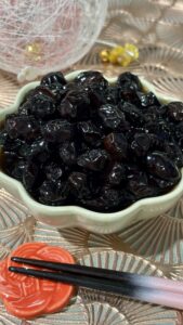 Traditional Japanese Kuromame (sweet black soybeans) simmered in soy sauce and sugar, a glossy Japanese New Year dish served as part of Osechi Ryori.日本のおせち料理の一品、砂糖と醤油で煮た伝統的な黒豆（甘煮）。つやのある黒豆の和食家庭料理。